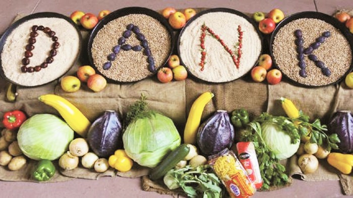 Bunte Früchte und Gemüse, arrangiert, um „DANKE“ zu buchstabieren, mit Getreide und Nüssen darüber.