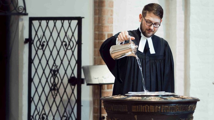 Ein Priester gießt Wasser in ein kunstvoll verziertes Becken in einer Kirche.