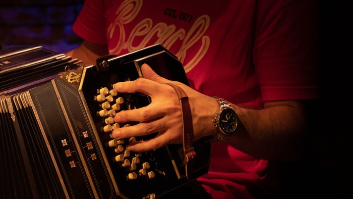 Detail eines Bandoneons, zu sehen sind die Knöpfe und eine Hand unter einem Lederriemen