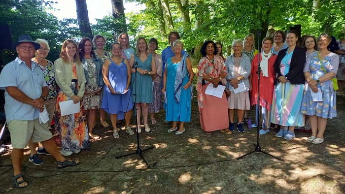 Gruppe af mennesker, der står udendørs og holder certifikater under en formel udendørs ceremoni eller anerkendelsesbegivenhed.
