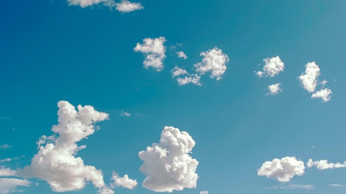 Heller blauer Himmel mit verstreuten, flauschigen weißen Kumuluswolken, die sich über den Horizont erstrecken.
