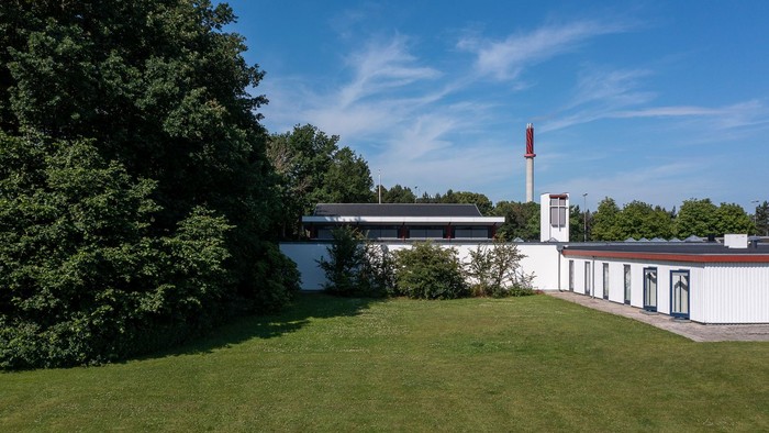 Moderne bygning omgivet af grønt under en klar blå himmel.