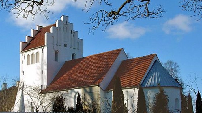 Et hvidt kirkebygning med røde tag og en klokketårn i en snedækked landskab