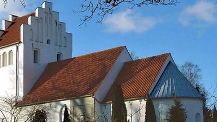 Et hvidt kirkebygningskompleks med røde tag og en tårn.