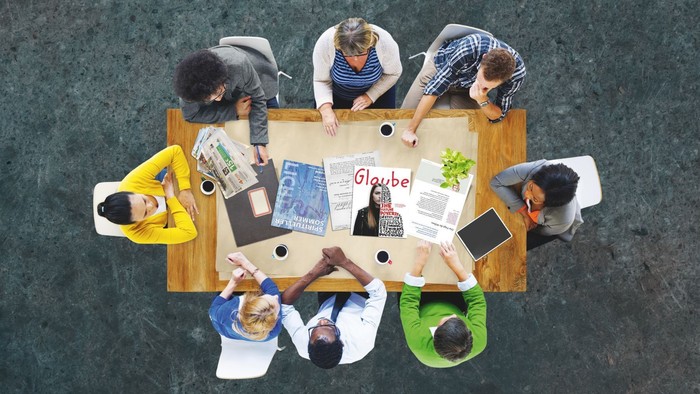 Eine Gruppe von Menschen sitzt um einen Tisch und arbeitet an Projekten.