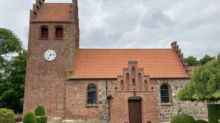 Historisk murstenskirke med klokketårn, omgivet af velplejet grønt og stenmure.