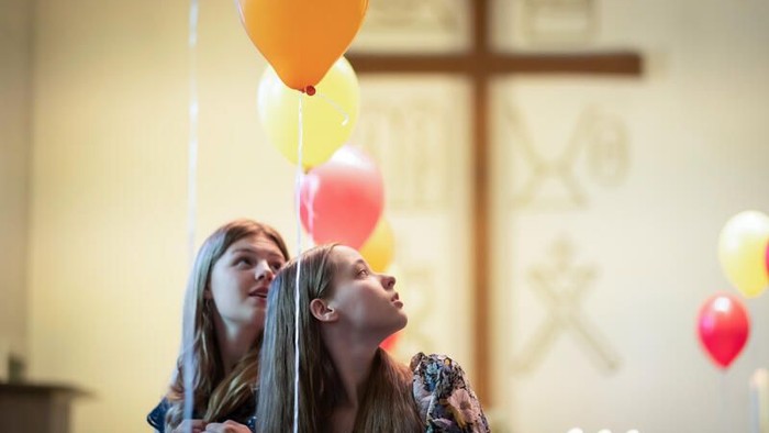 Zwei Personen schauen nach oben, während sie bunte Luftballons in einer Kirche halten.