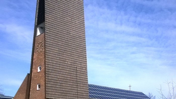 Das hohe Ziegelgebäude mit einem großen Kamin und Solarpaneelen auf dem Dach.