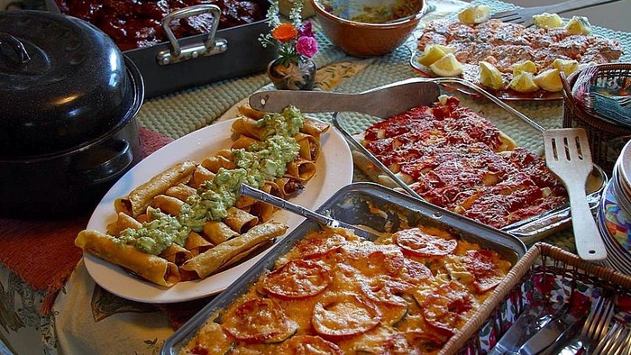 En buffetopsætning med tacos, lasagne, fyldte peberfrugter og andre lækre retter på fade.