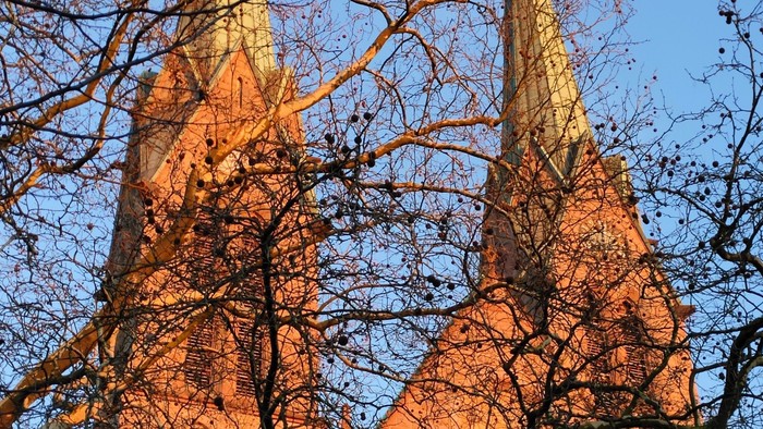 Goldene Kirchenspitzen, umhüllt vom warmen Sonnenlicht durch herbstliche Bäume vor einem klaren blauen Himmel.