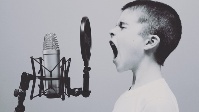 Ein junger Junge singt leidenschaftlich in ein Mikrofon mit offenem Mund.