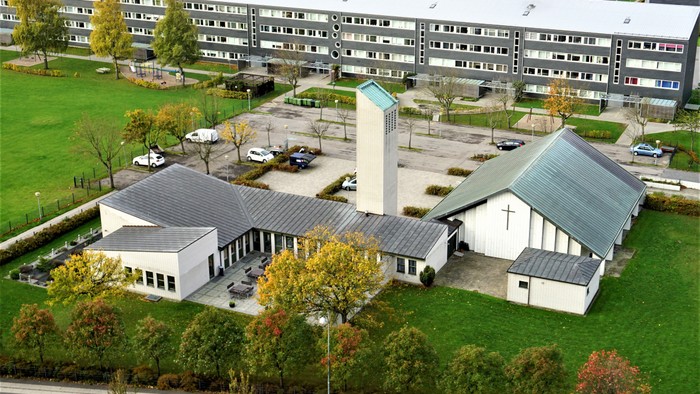 Moderne kirkekompleks omgivet af boligbygninger, parkeringsområde og grønne områder.