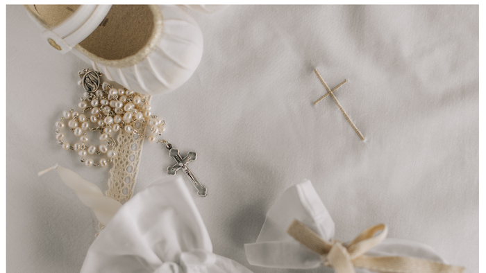 A white cloth embroidered with a cross; on top the cloth is a child's white satin shoe, the sleeve of a garment, a white tied pouch and a white rosery.