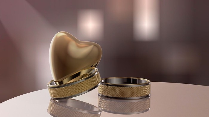 Ein goldenes Herz und zwei Ringe auf einer weißen Oberfläche