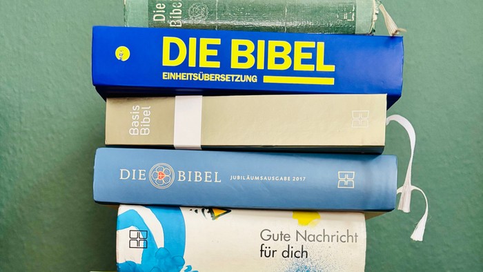 Stapel bunter deutscher Bibelausgaben und Kinderbibeln auf einem Regal.