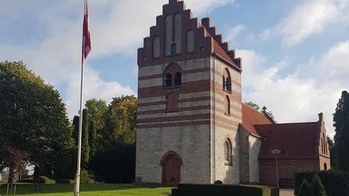 En kvinde går forbi en historisk bygning med tårn og flagstang.