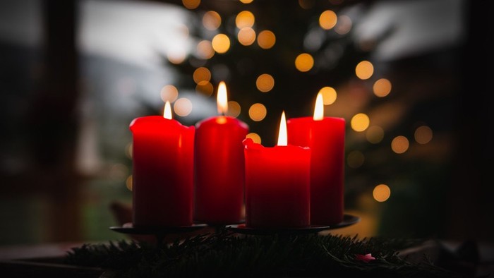 Drei brennende rote Kerzen vor einem Weihnachtsbaum