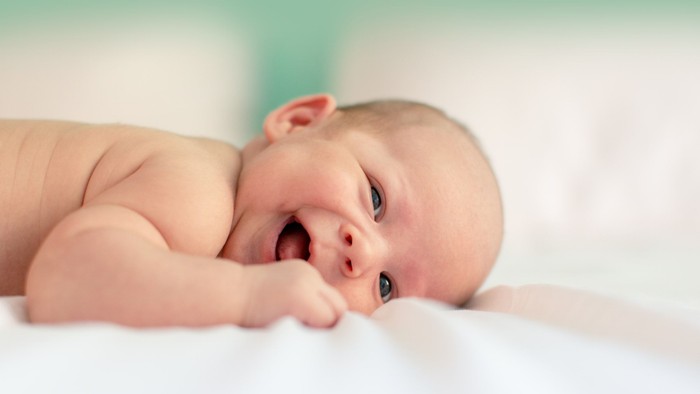 En nyfødt baby ligger på maven og suger på sin knyttede hånd med et fredfyldt udtryk.