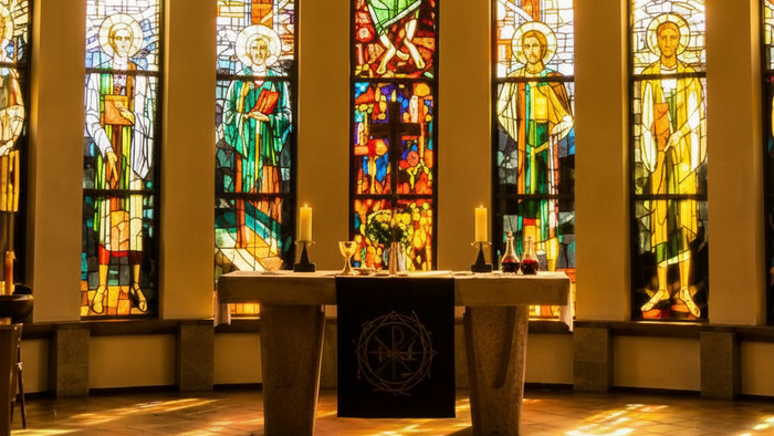 Eine helle warme Kirche mit bunten Kirchfenstern. In der Mitte eine Kanzel mit Abendmahlgeschirr