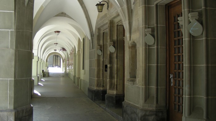 Ein langer, gewölbter Flur mit Holztüren und Wandleuchten.