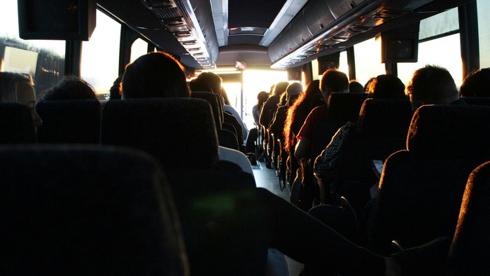 Businnenraum voller Fahrgäste, die in Reihen sitzen, von hinten betrachtet, mit einfallendem Sonnenlicht.