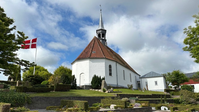 En hvid kirke med spiret og en dansk flag på en grøn plads