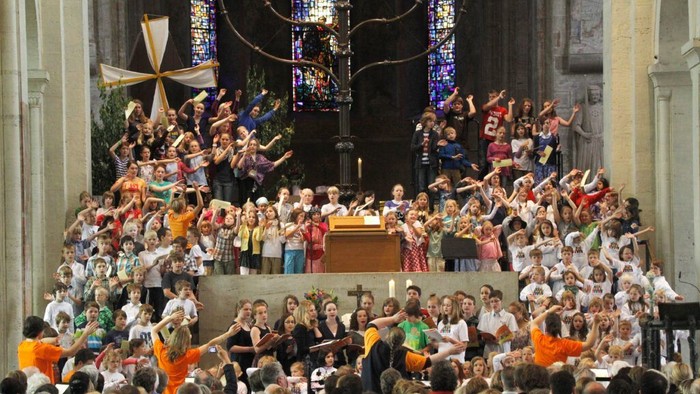 Große Menge von Kindern und Erwachsenen, die fröhlich singen und in einer prächtigen Kathedrale auftreten.