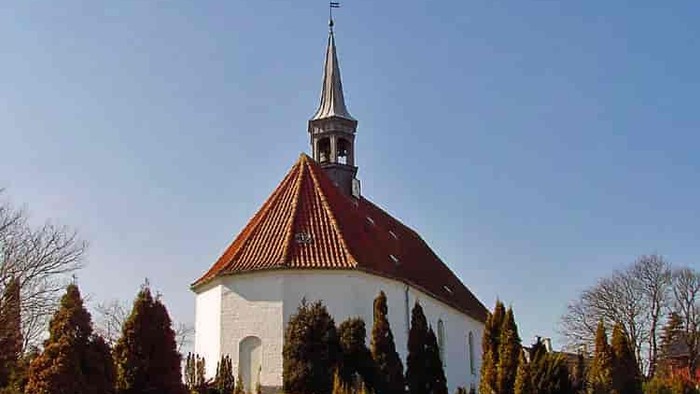En hvid kirke med rødt tag og spir med kryds i en parkagtig omgivelse