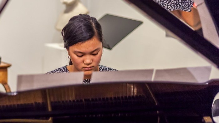 En kvinde spiller piano i et rum med en buste på en bordsplank.