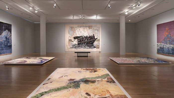 Moderne Kunstausstellung mit großen abstrakten und landschaftsstilistischen Gemälden, die auf Holzböden präsentiert werden.