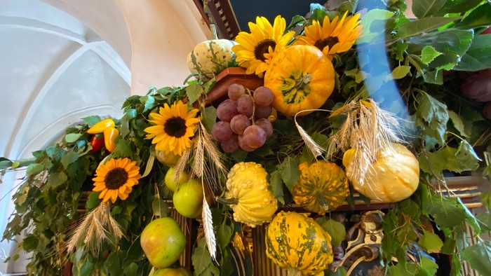 Farverigt efterårs-høstarrangement med solsikker, græskar, druer, æbler og hvedeneg.
