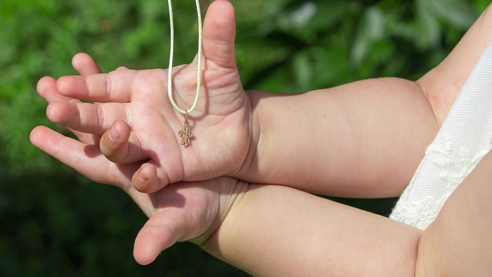Ein Baby hält eine Kette mit Kreuz-Anhänger in der Hand.