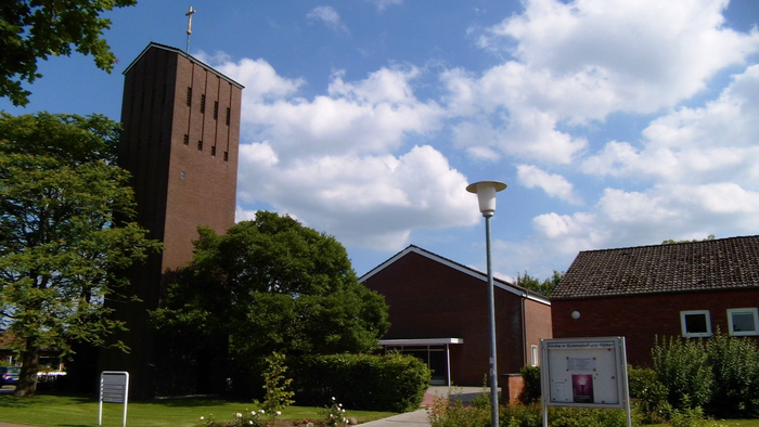 Ein ruhiger Kirchenkomplex mit einem hohen Backsteinturm, umgeben von Grünflächen und klarem blauem Himmel.