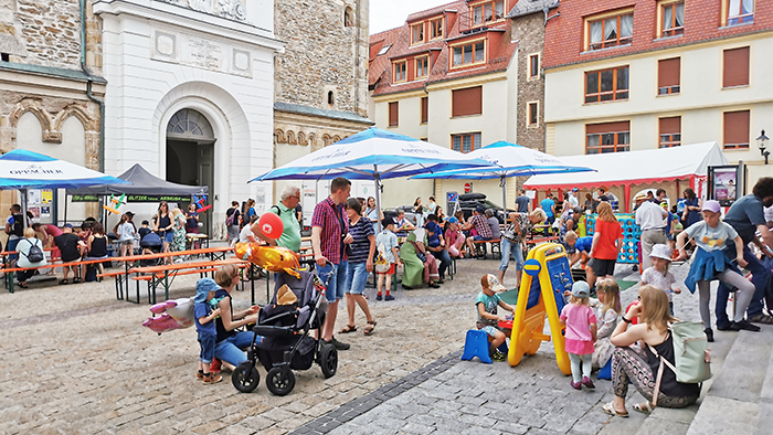Marktplatz mit vielen Menschen und Kindern, bunte Spielzeuge und Sonnenschirme