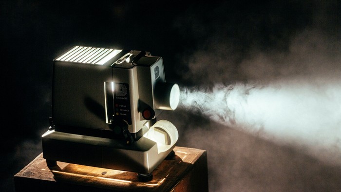 Vintage-Filmprojektor, der Licht und Rauch auf eine dunkle Oberfläche wirft.