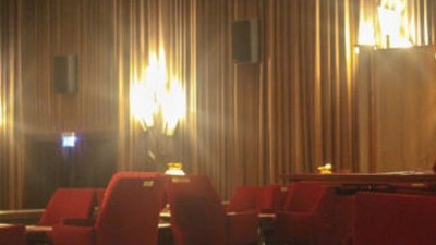 Vintage-Theaterinnenraum mit roten Sitzen, gedämpftem Licht und verzierten Wandlampen.
