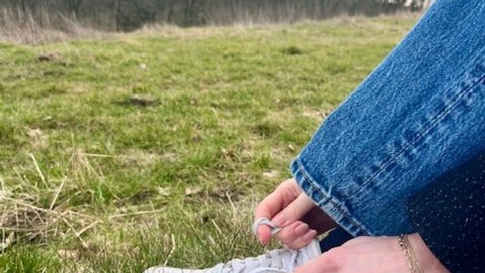 Person binder en sneaker i et græsklædt udendørsområde med træer i baggrunden.