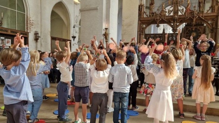 Kinder tanzen in einem großen Raum mit Erwachsenen.