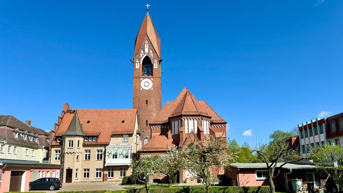 Bild zeigt eine Kirche mit hohem Turm und Uhr, umgeben von einem gepflegten Garten.