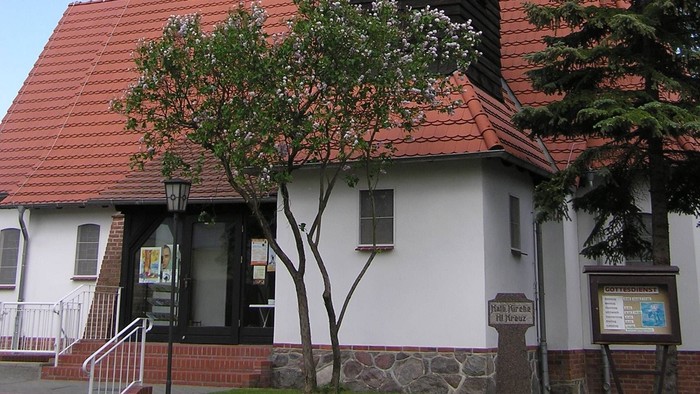 Kirchengebäude mit hohem Turm und rotem Dach, umgeben von Bäumen