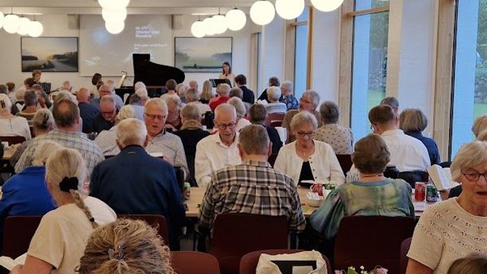 En stor gruppe mennesker samledes i en rummelig spisesal og nød et måltid sammen.