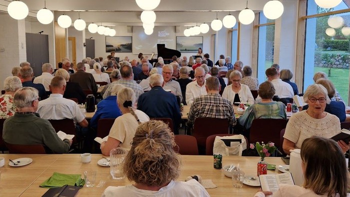 En stor gruppe mennesker samledes i en rummelig spisesal og nød et måltid sammen.