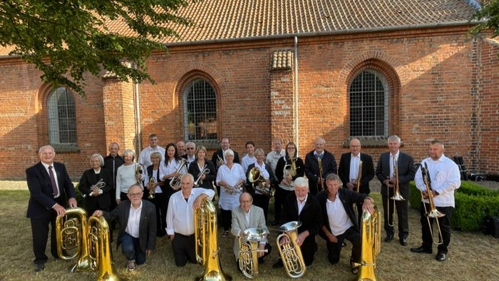 En gruppe musiker poserer med instrumenter i forgrunden af en kirke