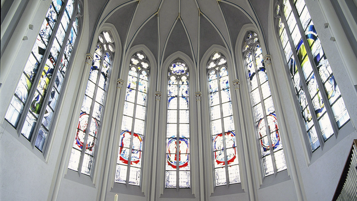 Hoch aufragende Kirchenfenster mit bunten Glasmalereien und Altar davor