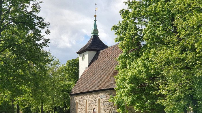 Historische Steinkirche, eingebettet zwischen üppigen grünen Bäumen mit einem kleinen Glockenturm.