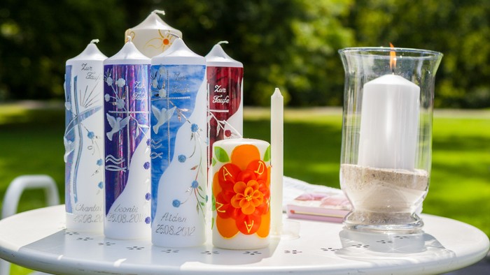 Verzierte Kerzen und ein sandgefüllter Votivhalter auf einem Gartentisch mit Blumenmustern.