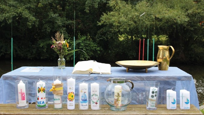 Geschmückter Außentisch mit Kerzen, Gläsern, Blumen und rituellen Gegenständen, arrangiert auf einem Tuch.