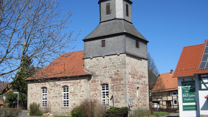 Außenansicht der evangelischen Kirche in Nothfelden. Natursteingebäude mit rotem Ziegeldach und Turm mit schieferverkleideter Haube.