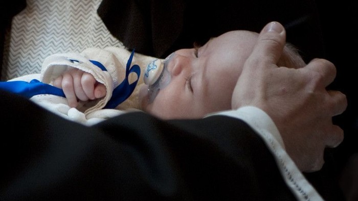 Nyfødt baby sover fredeligt, mens den blidt holdes af en voksens hånd.
