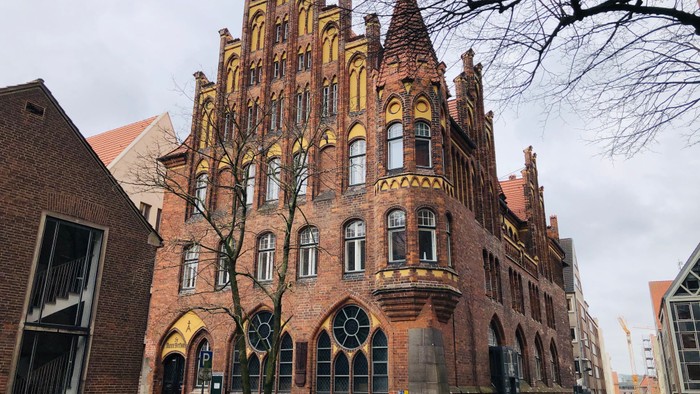 Altes Backsteingebäude mit spitzen Türmen und großen Fenstern an der Straße